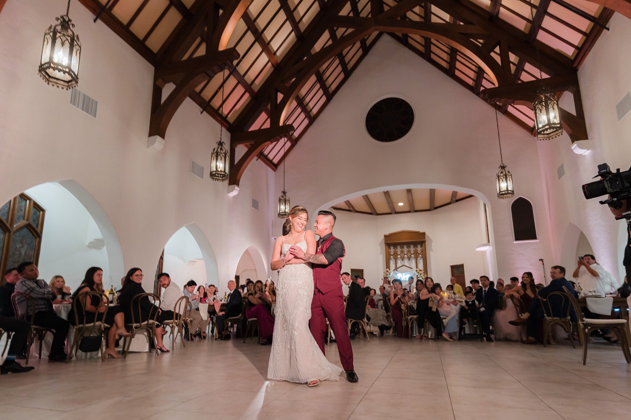 Bride and groom's first dance in cathedral reception hall with exposed beam ceiling and hanging lanterns