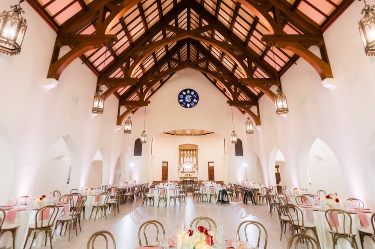 Wedding reception setup with exposed beam ceiling, hanging lanterns, and Gothic architecture at The Sanctuary featuring round tables with blush accents