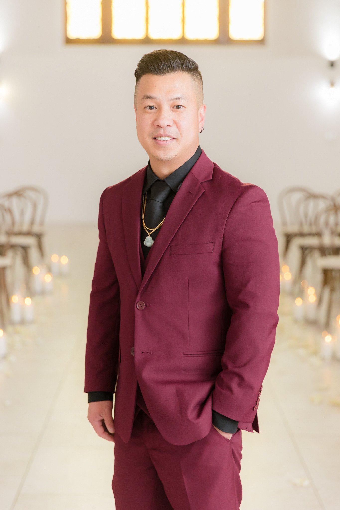 Groom wearing burgundy suit with black shirt and gold necklace at The Sanctuary wedding venue in Long Beach California