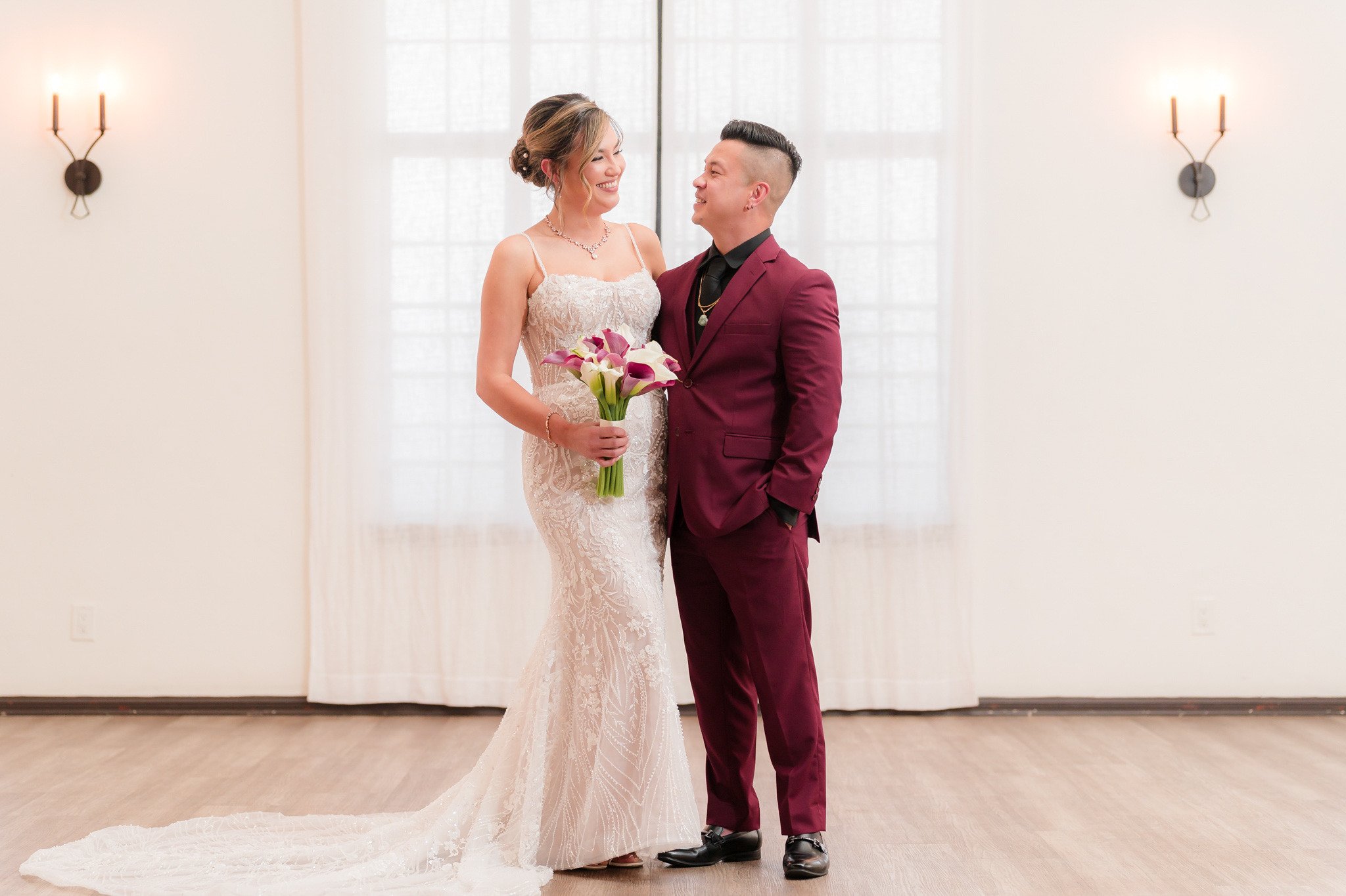 Bride in fitted lace wedding dress and groom in burgundy suit sharing romantic moment at The Sanctuary wedding venue