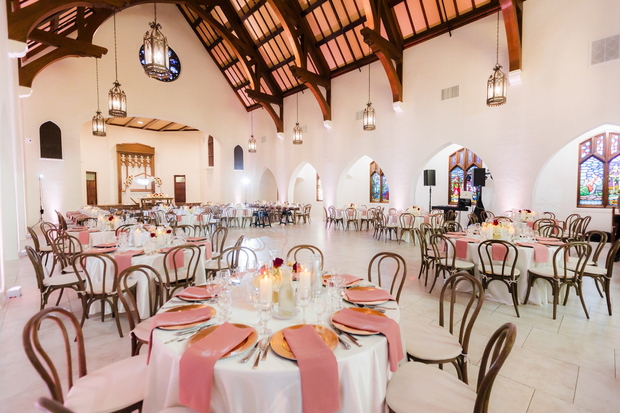 Wedding reception setup with white linens, blush pink accents, Gothic architecture, and hanging lanterns at The Sanctuary