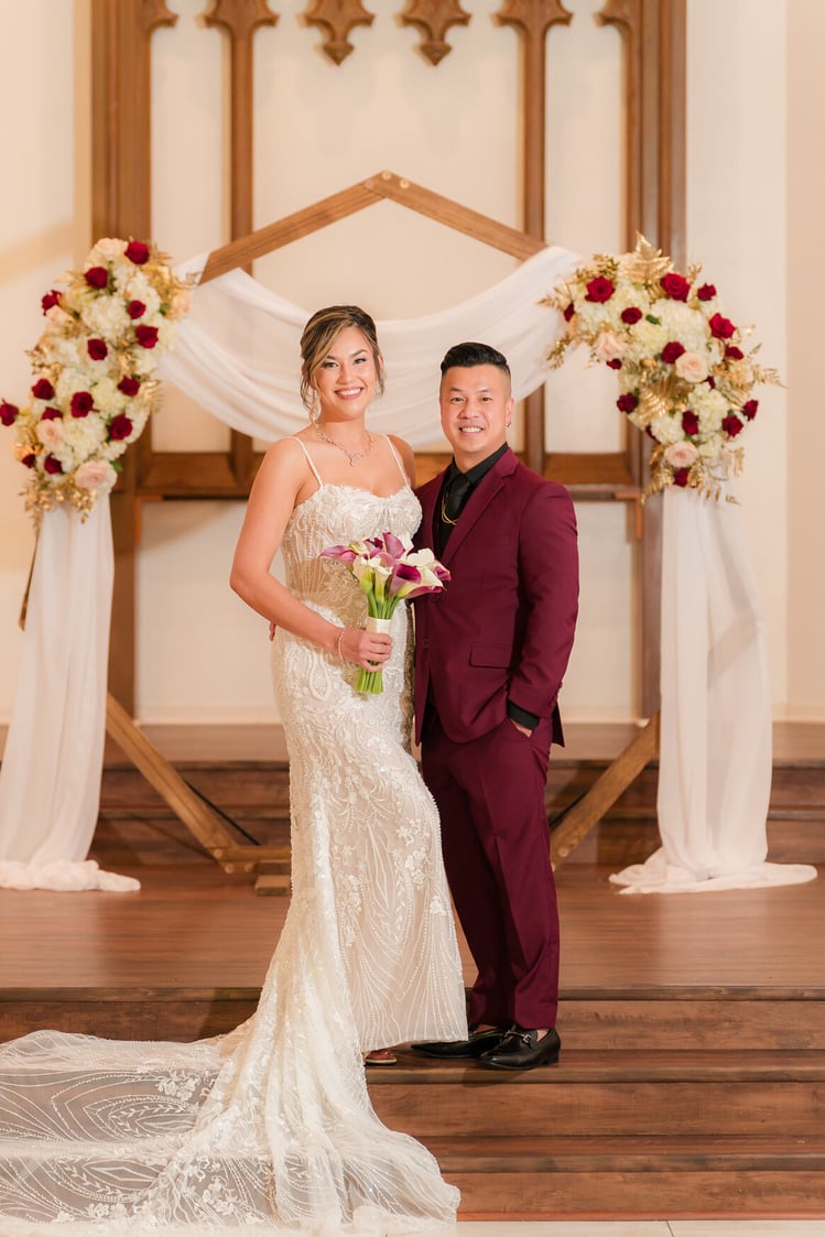 Wedding ceremony setup with white draping, burgundy roses, and cream floral arrangements against Gothic wooden architecture