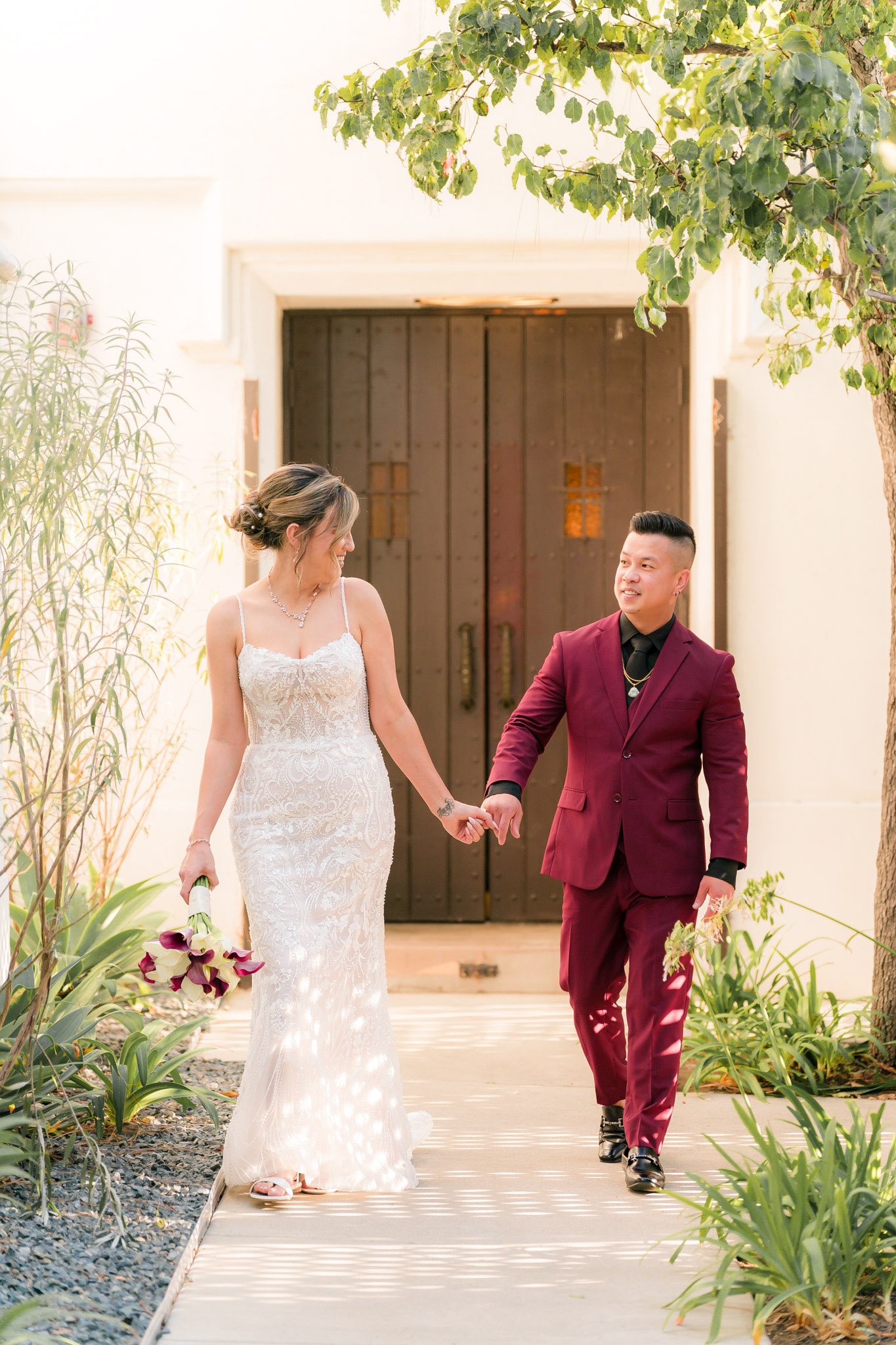 Bride and groom walking hand in hand through The Sanctuary's pathway with dappled sunlight