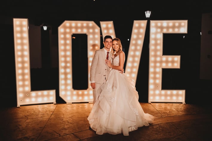 Maria & Hayden standing in front of the marquee love letters outside Fallbrook Estate