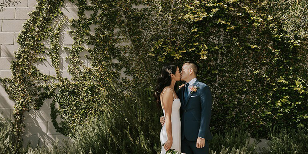 Couple kissing in front of ivy at The Harper by Wedgewood Weddings