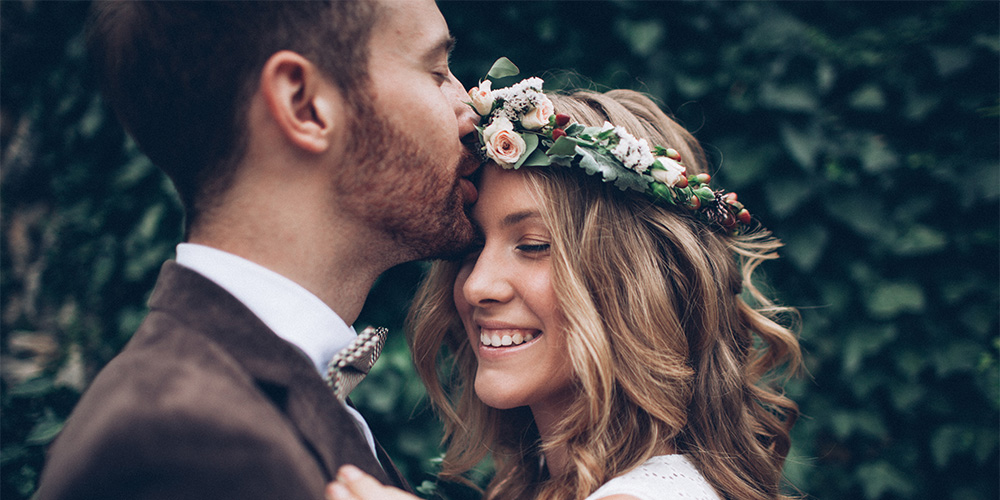 Happy couple, groom kissing bride on forehead. Bride with flowers in her hair