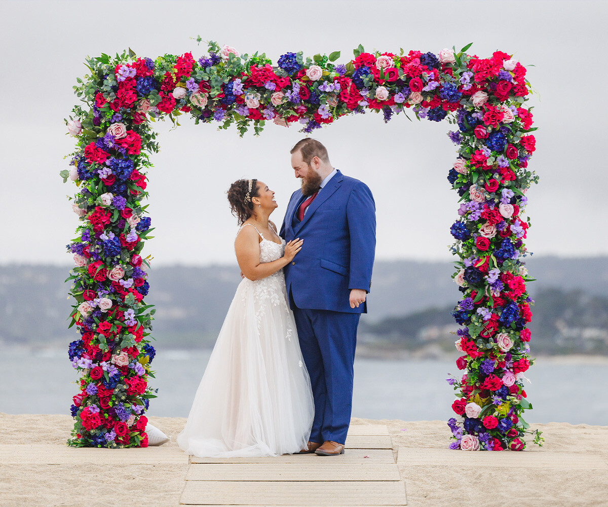 Couple in front of arch with dramatic bright florals - Carmel Fields by Wedgewood Weddings