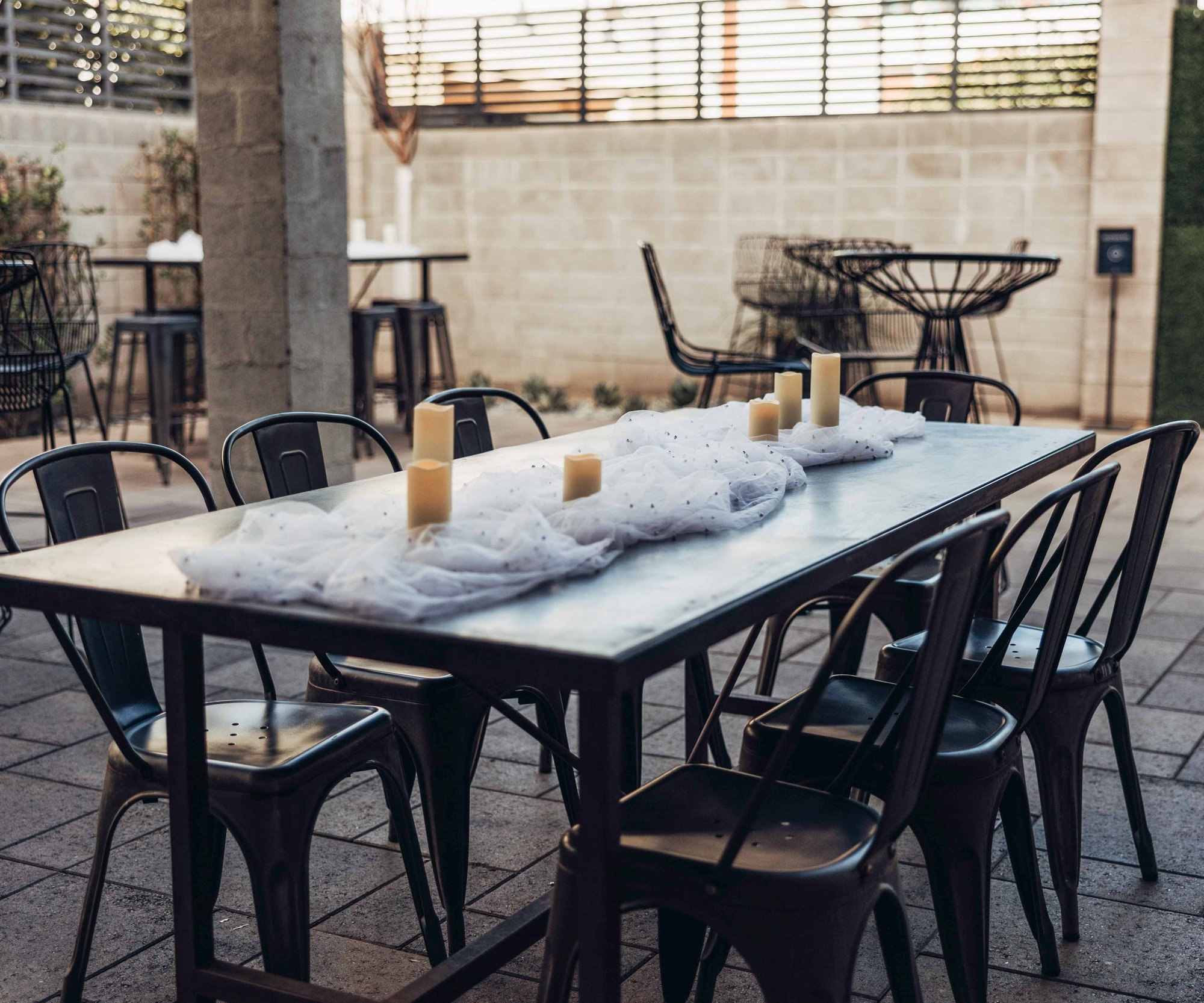 Outdoor cocktail hour table at Croft Downtown Phoenix with black metal chairs, white tulle runner, and cream candles under covered patio