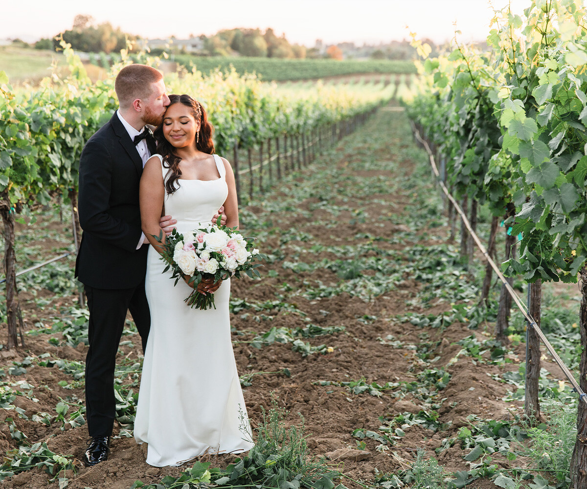 Newlyweds kissing among vines - Danza del Sol Winery by Wedgewood Weddings