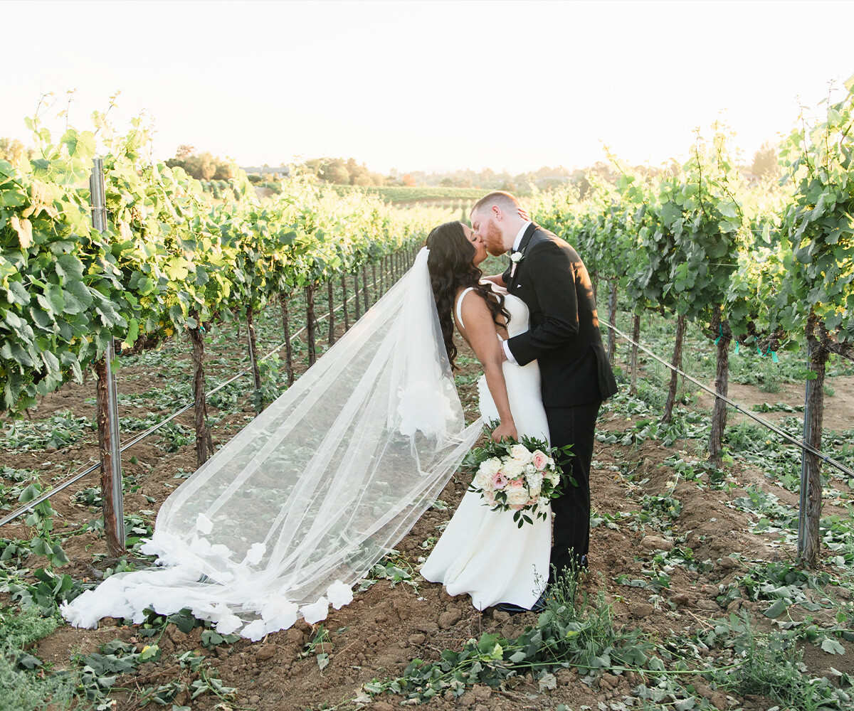 Newlyweds kissing among vineyards - Danza del Sol Winery by Wedgewood Weddings