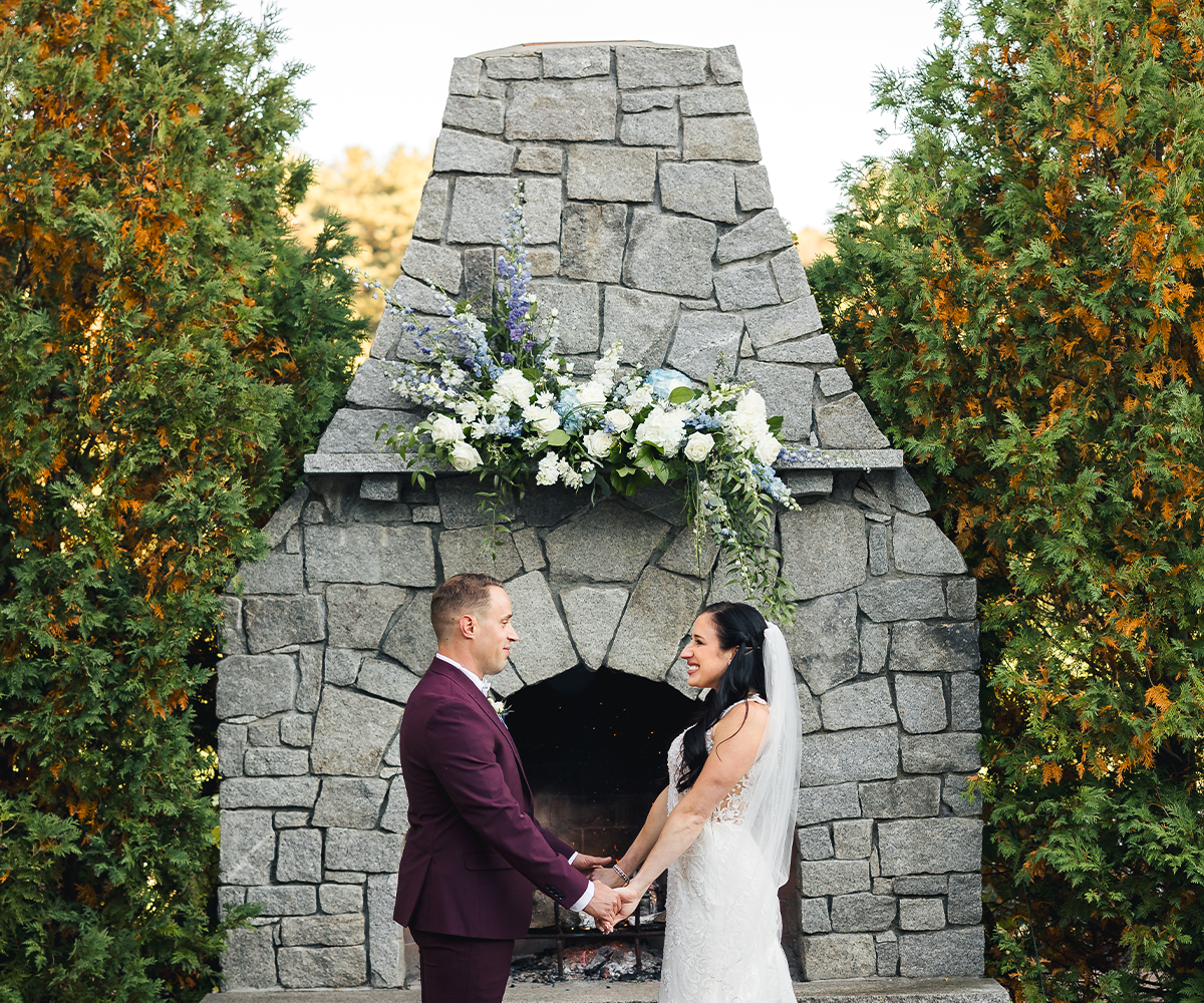 Newlyweds holding hands in front of fireplace ceremony site - Groveland Fairways by Wedgewood Weddings