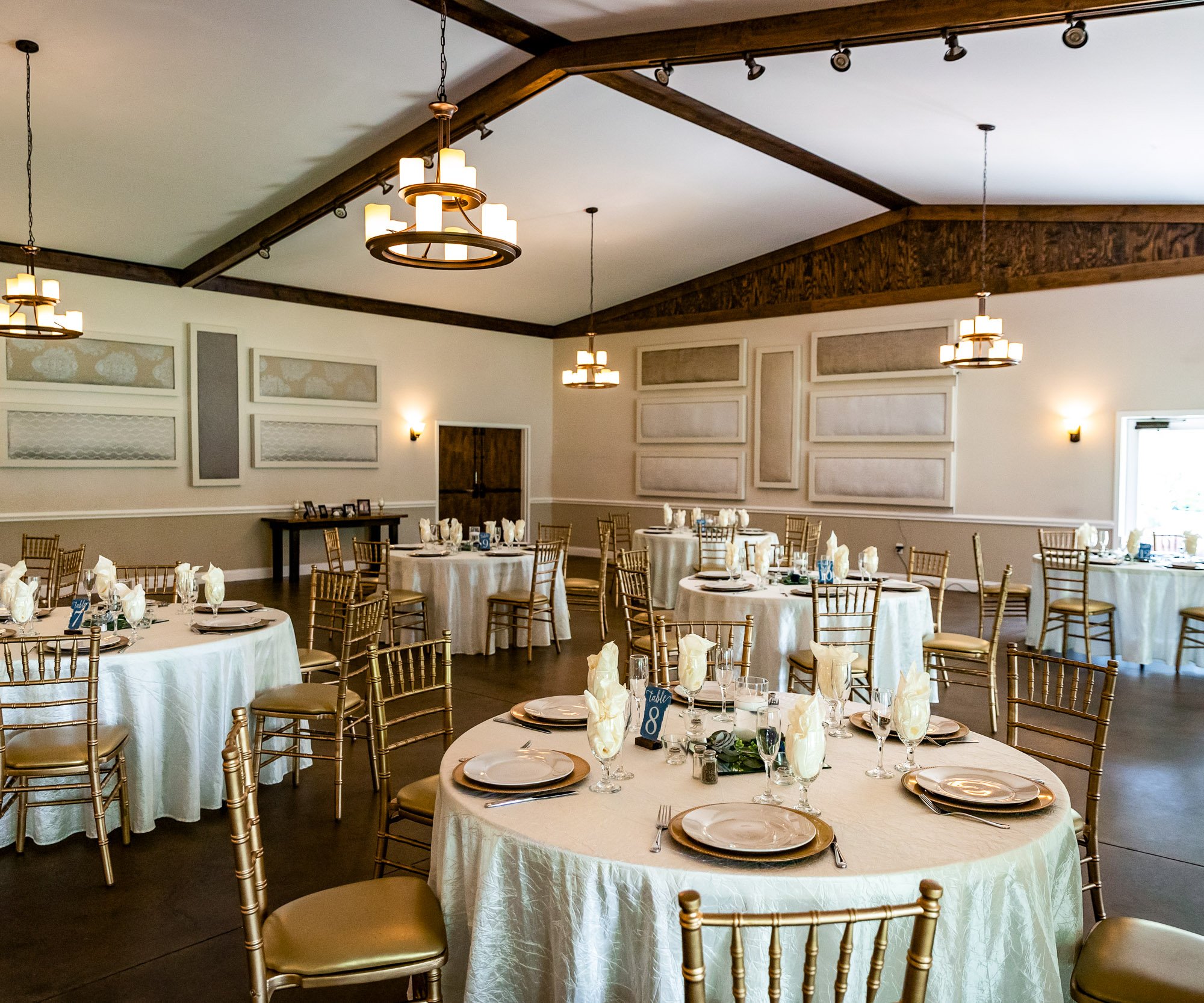 Wedding reception details in Riverwood Manor's Grand Hall showing decorative wall panels, wooden ceiling beams, and formal table settings with white linens and gold chairs - Ken Thomas Photography