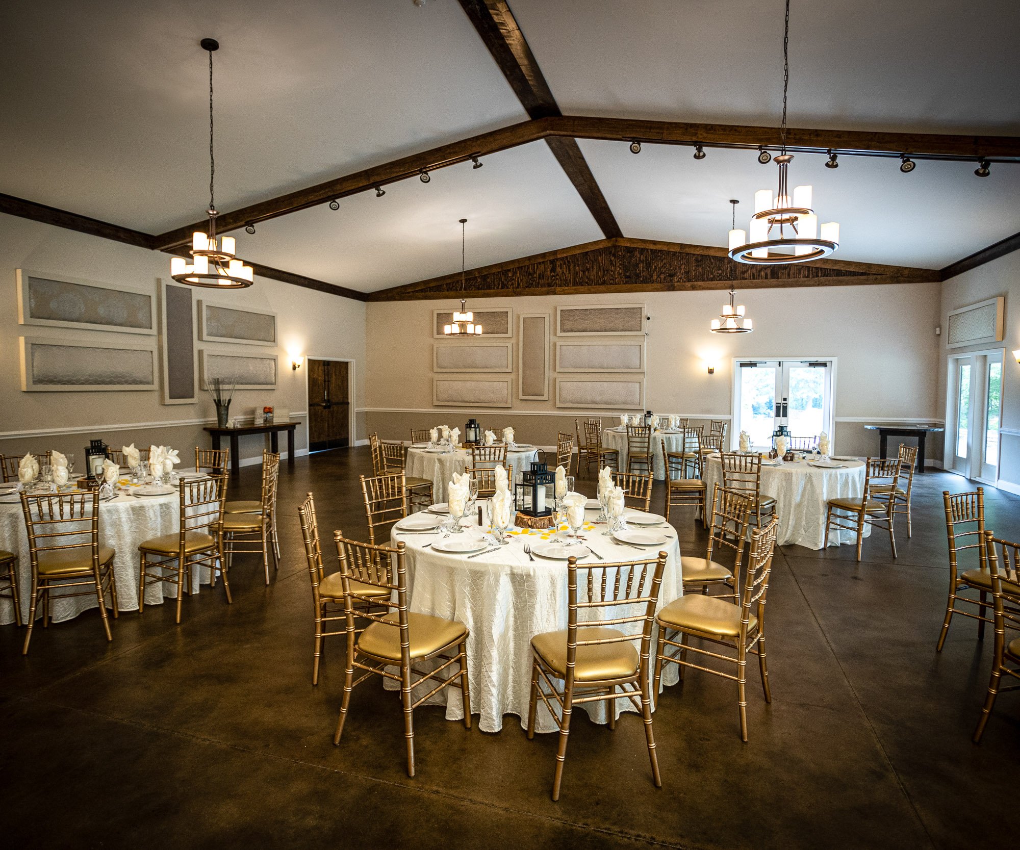 Elegant wedding reception setup in Riverwood Manor's Grand Hall featuring vaulted ceilings with wooden beams, chandeliers, white linens and gold chiavari chairs - Ken Thomas Photography