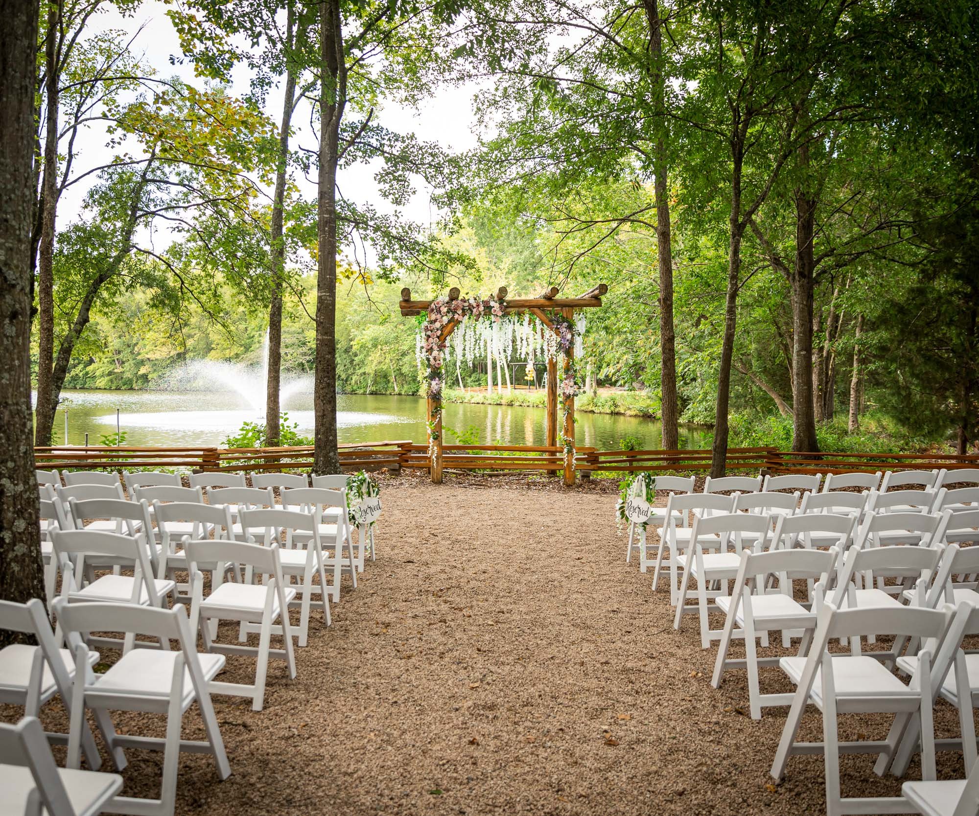 Intimate forest wedding ceremony setup at Riverwood Manor with wooden arbor decorated with floral arrangements, white chairs, and natural woodland backdrop - Ken Thomas Photography