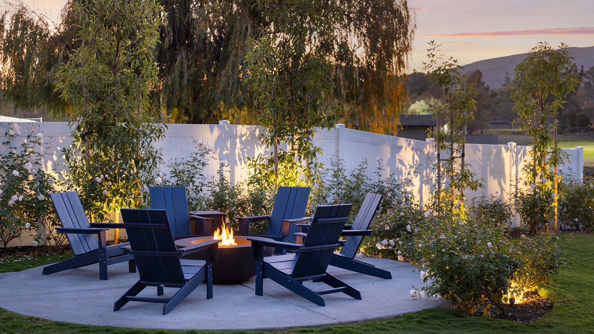 Evening Fire Pit Lounge Area with Adirondack Chairs and Garden Backdrop at Sunset