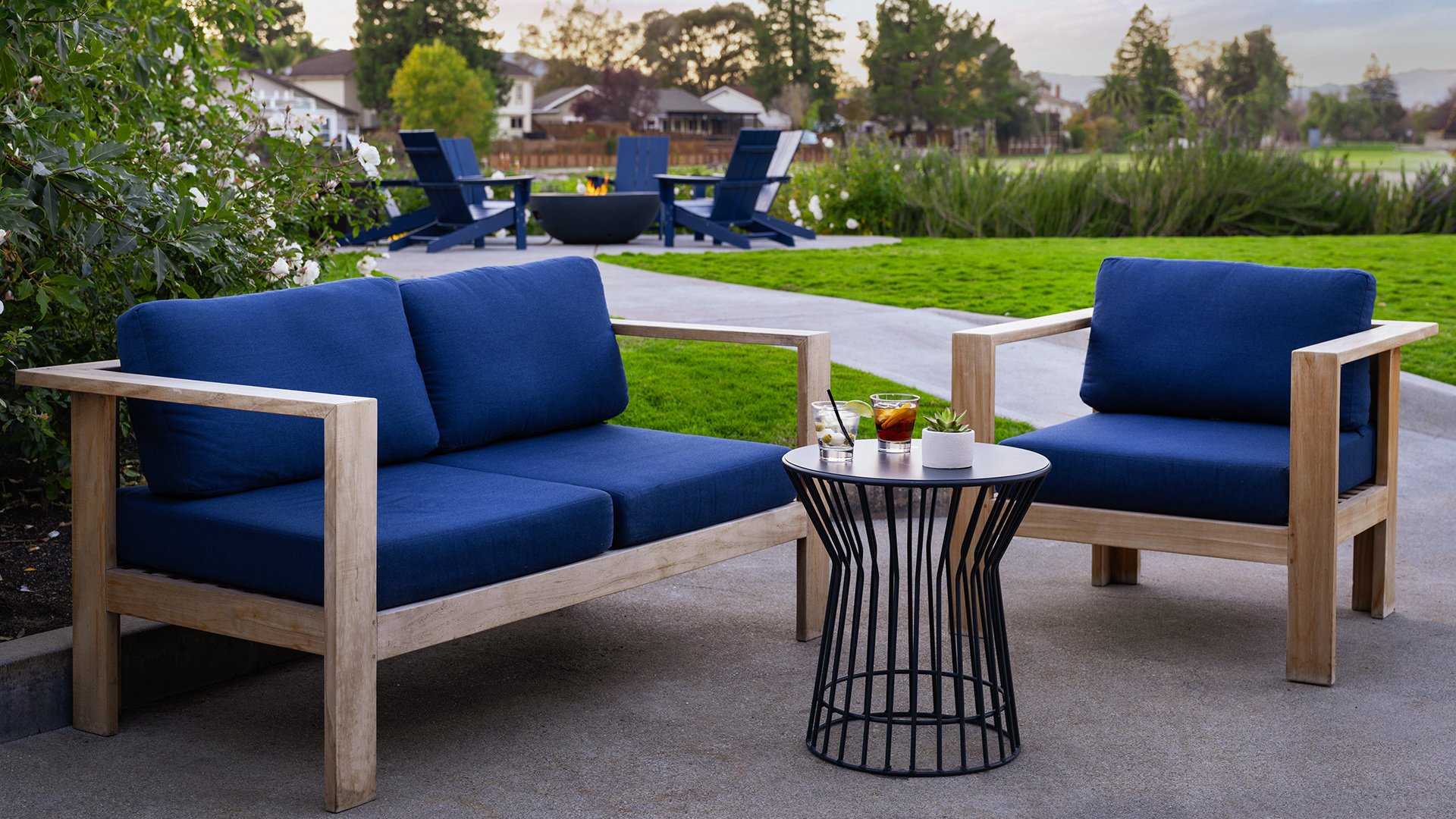 Modern Outdoor Lounge Area with Navy Blue Seating and Cocktail Tables Against Garden Setting