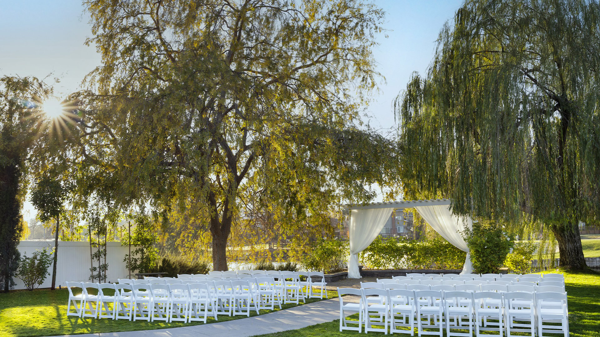 Outdoor Garden Wedding Ceremony Site with White Draped Pergola and Willow Tree Backdrop