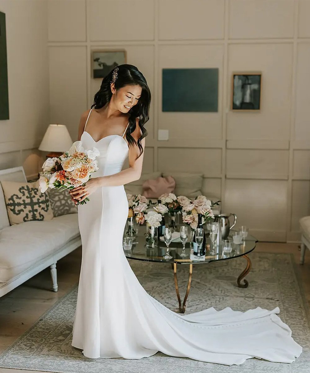 Bride in elegant fitted wedding dress with peach bouquet in The Harper's bright Sunroom featuring modern wall paneling and French-inspired decor