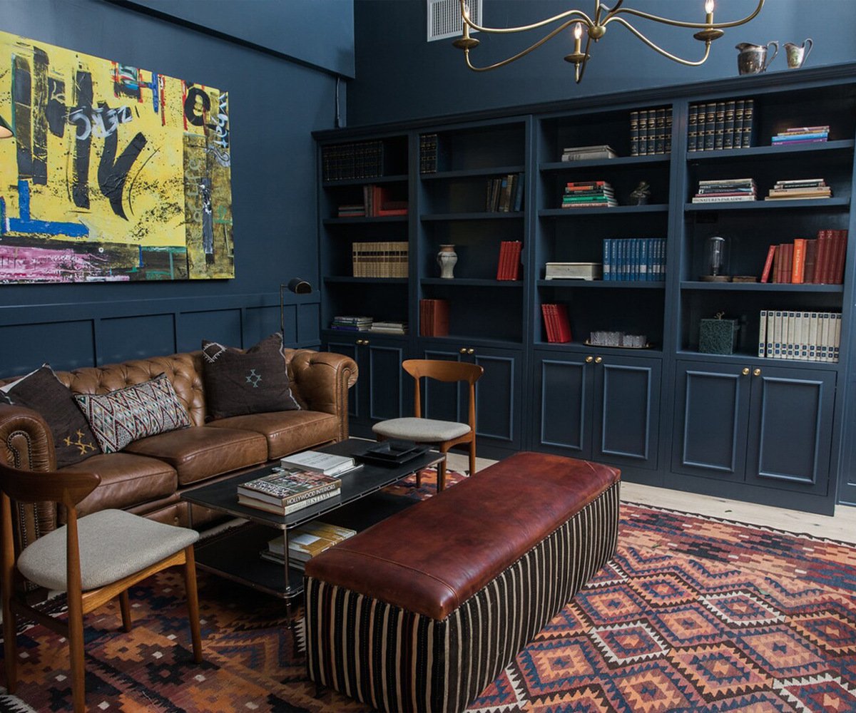 Stylish library lounge at The Harper with navy built-ins, leather furnishings, modern art, and geometric rug - perfect for wedding party preparations