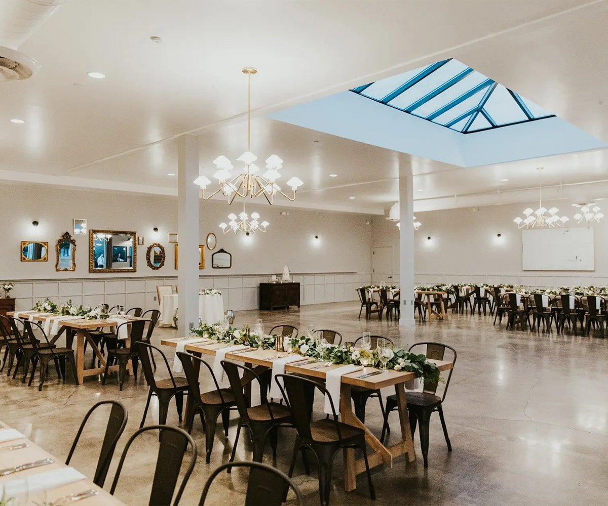 Industrial-chic reception hall at The Harper with skylight, ornate mirrors, farmhouse tables, and metal chairs - modern Costa Mesa wedding venue