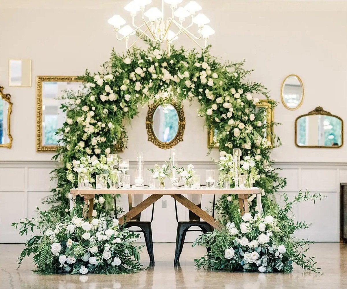 Elegant sweetheart table at The Harper with dramatic white floral arch, vintage gold mirrors, and candlelit table setting - Costa Mesa wedding venue