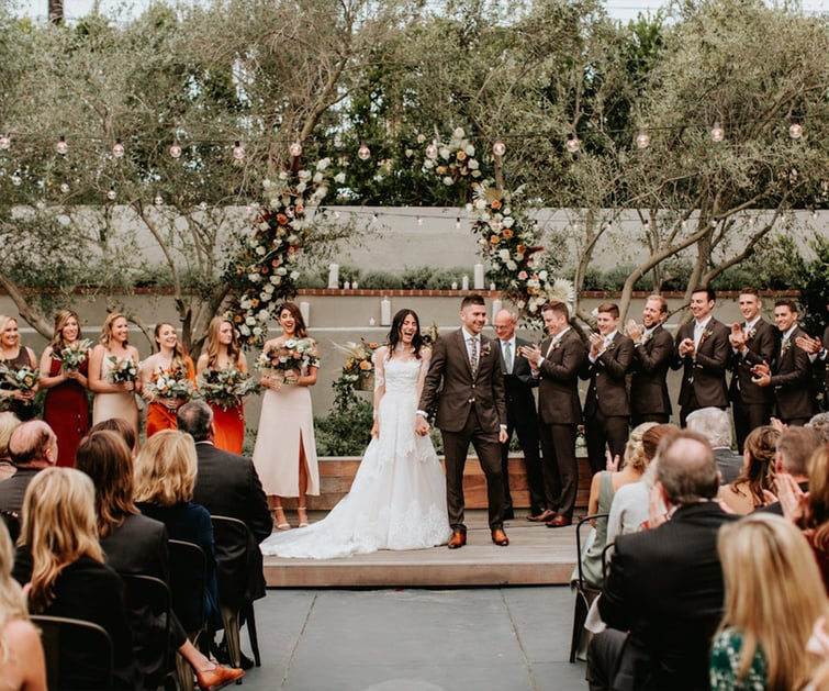 Garden wedding ceremony at The Harper with floral arch, string lights, and olive trees - modern Costa Mesa wedding venue