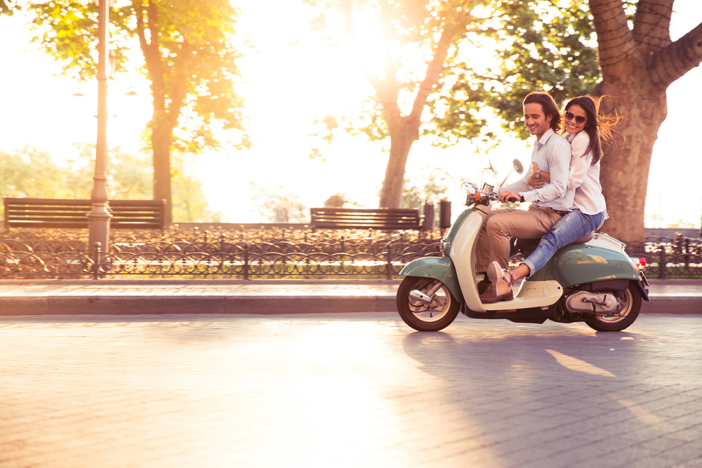 Cheerful young couple riding a scooter and having fun. Sun is shining in the morning