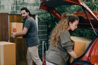 Couple loading cardboard boxes into a car trunk while preparing for a move